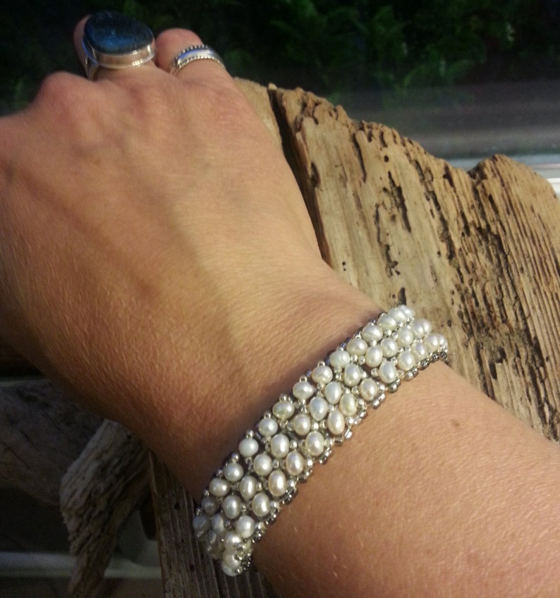 May include: A white pearl bracelet with multiple rows of pearls. The bracelet is made with small, round pearls and silver beads.