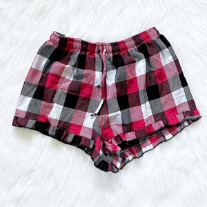 Puede incluir: Pantalones cortos de pijama de cuadros rojos, negros y blancos con un dobladillo con volantes.