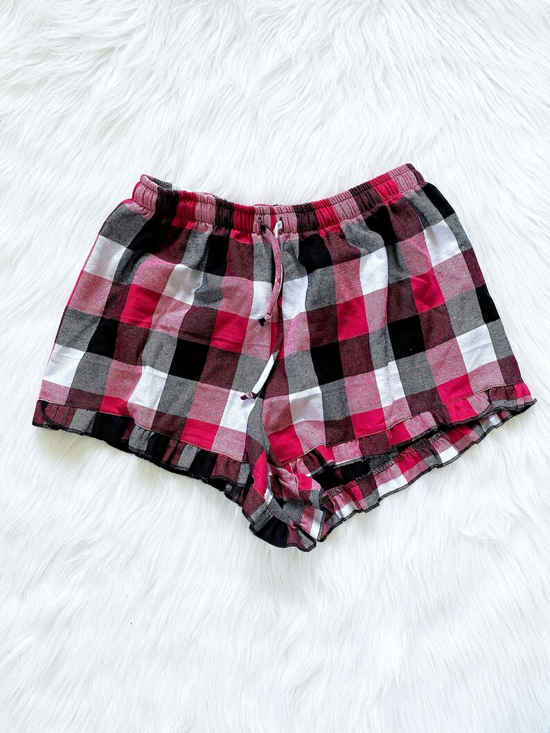 Puede incluir: Pantalones cortos de pijama de cuadros rojos, negros y blancos con un dobladillo con volantes.