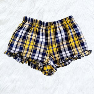 Puede incluir: Shorts de cuadros amarillos y azules con un dobladillo con volantes.