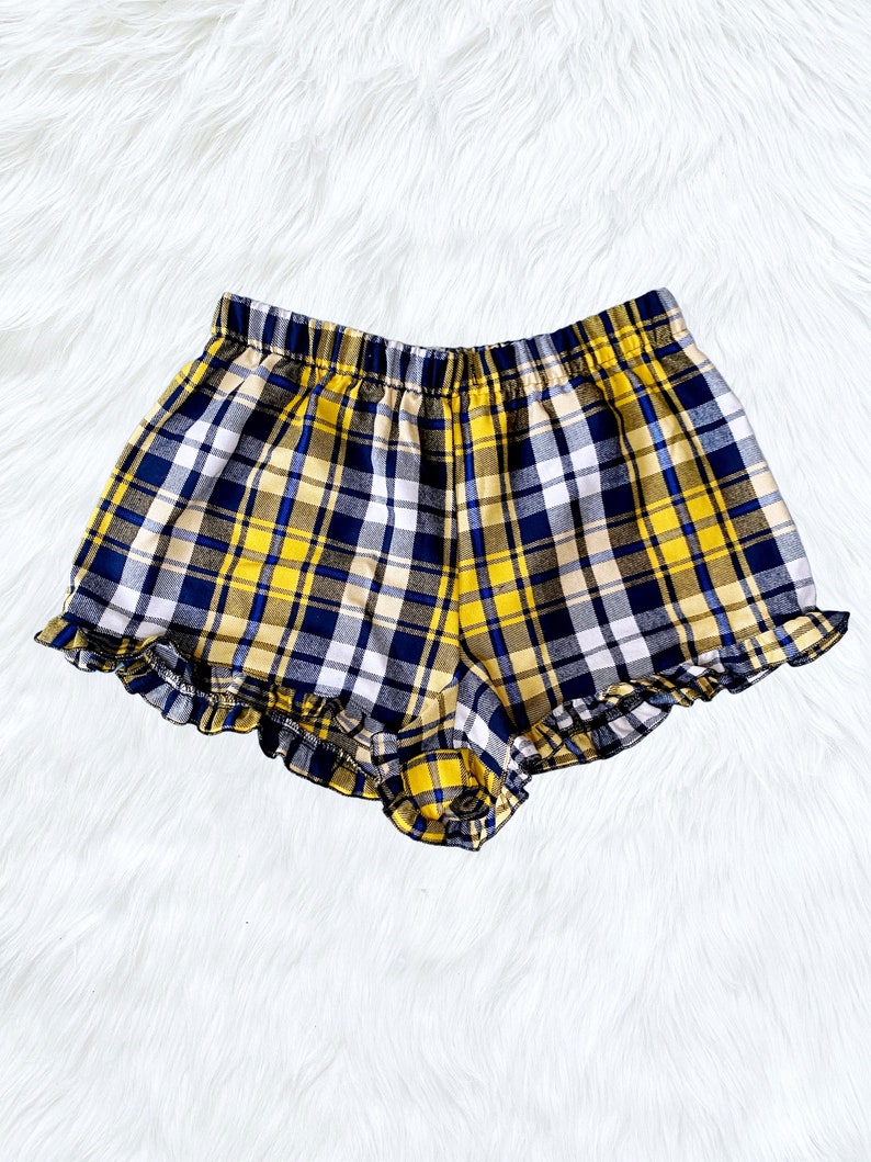 Puede incluir: Shorts de cuadros amarillos y azules con un dobladillo con volantes.