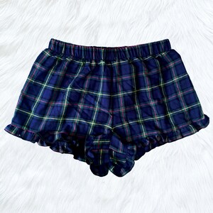 Puede incluir: Pantalones cortos de pijama de cuadros azules y verdes con un dobladillo con volantes.