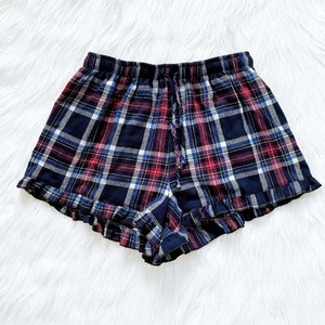 Puede incluir: Pantalones cortos de pijama a cuadros azules, rojos y blancos con un dobladillo con volantes.