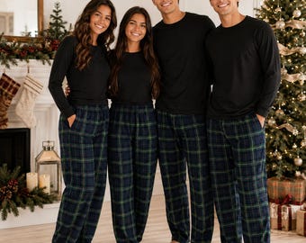 May include: Four individuals wearing matching long-sleeved black crewneck shirts and navy blue, green, and white plaid pajama pants. The pants feature a classic tartan pattern with a straight-leg fit and side pockets, paired with solid black tops.