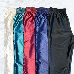 May include: Five pairs of satin pants in different colors: ivory, teal, burgundy, navy blue, and black.