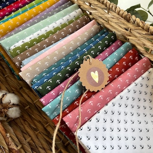 May include: A stack of fabric swatches featuring various anchor patterns. The swatches are in a range of colours, including white, blue, green, red, and brown. The fabric is displayed in a basket.