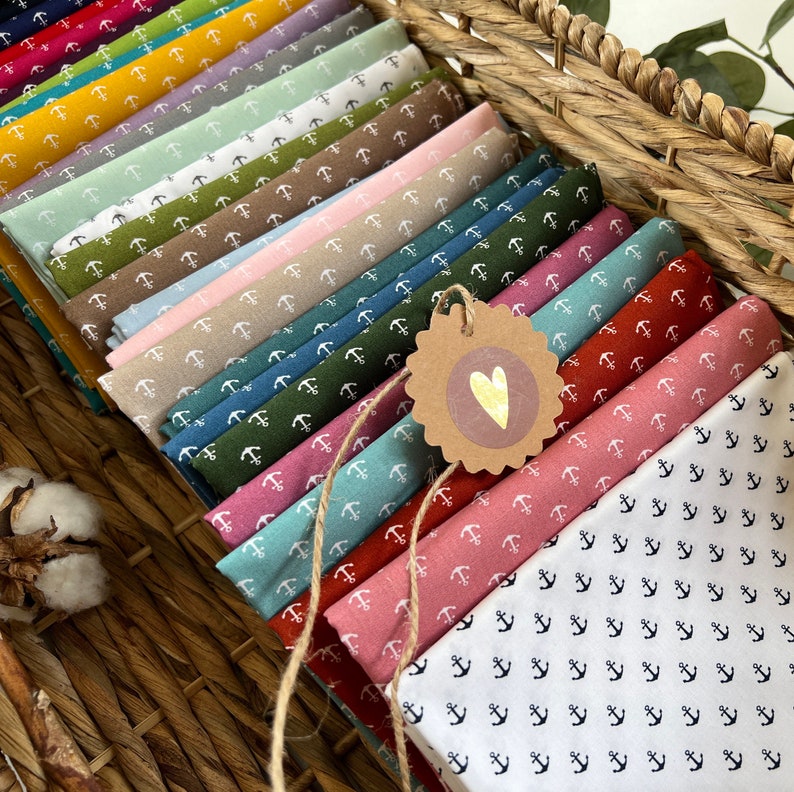 Op de afbeelding: Een stapel stofstalen met verschillende ankerpatronen. De stalen zijn in verschillende kleuren, waaronder wit, blauw, groen, rood en bruin. De stof is in een mand gelegd.