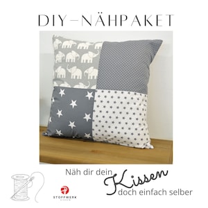 May include: DIY sewing kit for a grey and white cushion with a patchwork design featuring elephants and stars. The kit includes fabric, instructions, and thread. The text on the image reads "DIY - NÄHPACKET Näh dir dein Kissen doch einfach selber".