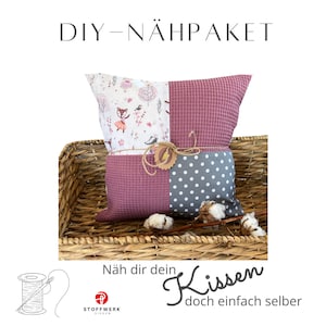 Könnte beinhalten: DIY-Nähpaket für ein Kissen mit einem rosa, grauen und weißen Blumenmuster. Das Paket beinhaltet Stoff, Garn und Anleitung. Der Text auf dem Bild lautet "DIY-NÄHPACKET Näh dir dein Kissen doch einfach selber".