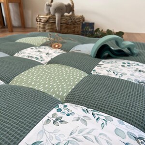 a close-up view of a quilt with a patchwork design, including a wicker basket, a stuffed elephant toy, and a wooden toy.