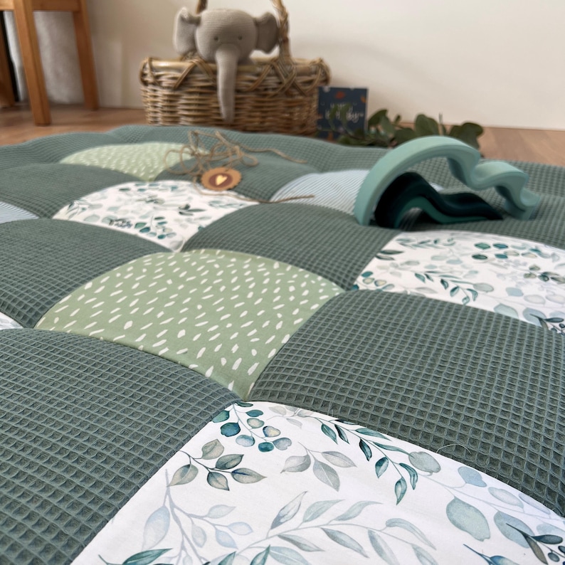 a close-up view of a quilt with a patchwork design, including a wicker basket, a stuffed elephant toy, and a wooden toy.