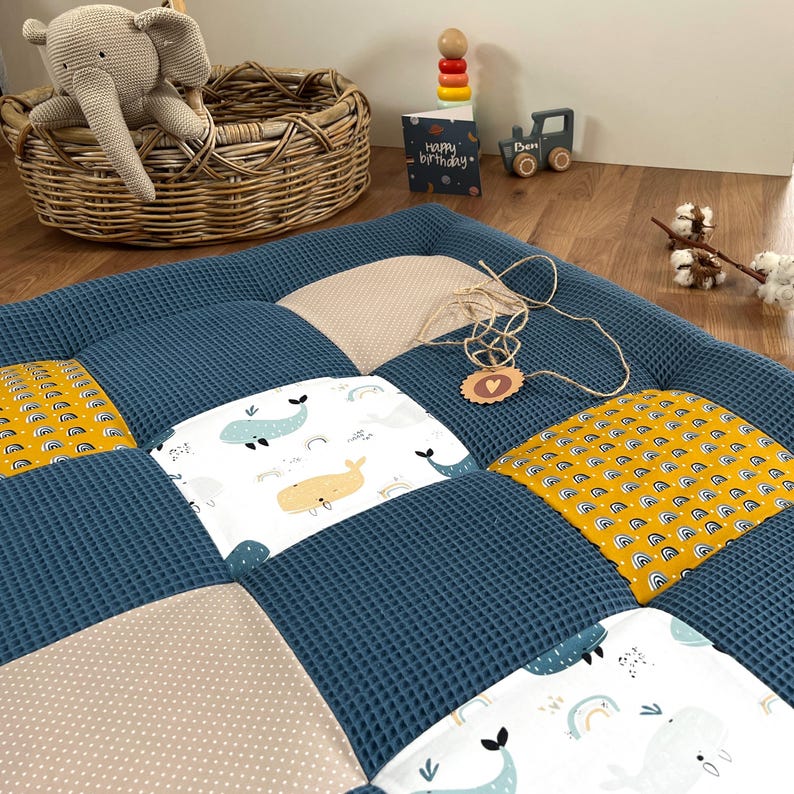 a cozy and colorful baby bedding set, including a blue and yellow quilt, a stuffed elephant, and a wooden toy car. The bedding set is placed on a wooden floor, with a wicker basket nearby.