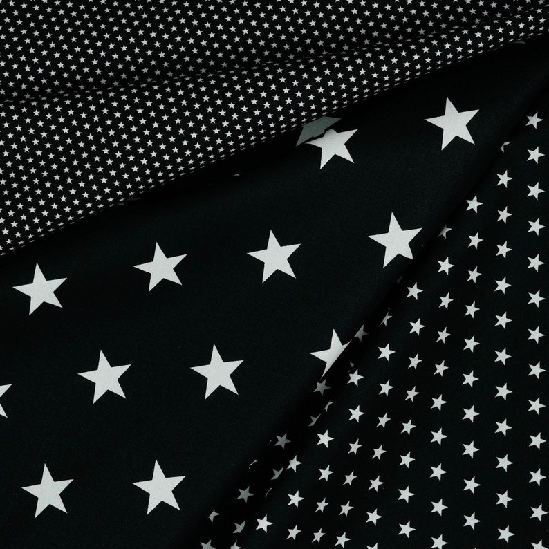 May include: Black fabric with white stars of different sizes. The fabric has a pattern of small white stars on one side and larger white stars on the other side.