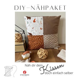 Könnte beinhalten: DIY Nähpaket für ein Kissen mit Patchwork-Design aus braunem, weißem und orangefarbenem Stoff. Der Stoff hat einen Waldtier-Druck mit Bären, Füchsen und Eichhörnchen. Der Text "DIY - NÄHPAKET" befindet sich oben im Bild. Der Text "Näh dir dein Kissen doch einfach selber" befindet sich unten im Bild.