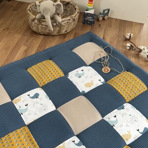 a cozy and colorful quilt with a patchwork design, placed on a wooden floor. The quilt has a mix of blue, yellow, and white colors, with various animal patterns such as elephants, dolphins, and rabbits. There is also a basket with a stuffed elephant toy and some toys, including a toy car and a toy train, scattered around the room.