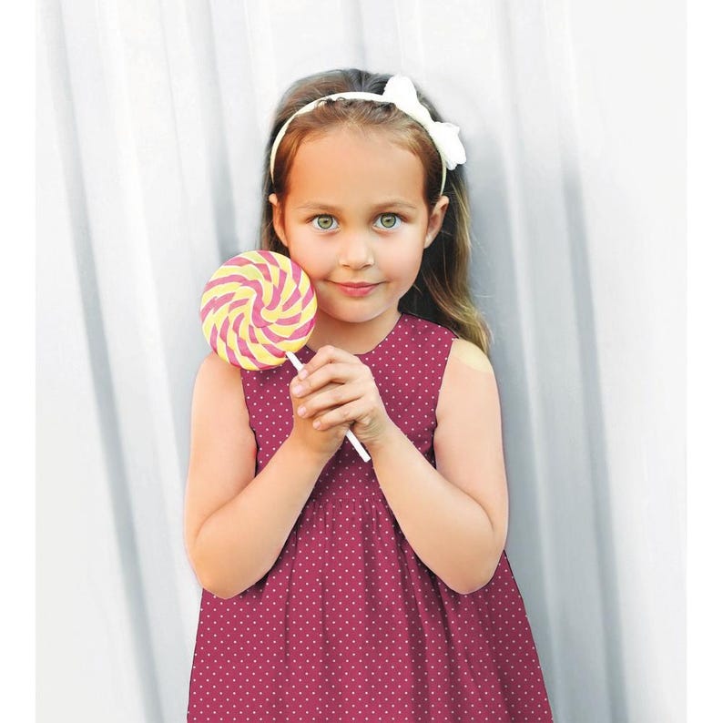 Pu&ograve; includere: Una bambina con un vestito rosa a pois e una fascia bianca tiene un lecca-lecca a spirale giallo e rosa.