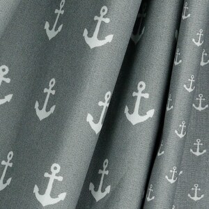 May include: Close-up of gray fabric with a repeating pattern of white anchors. The fabric is draped, showing folds and texture. The nautical theme is evident in the anchor design, suitable for home decor or apparel.