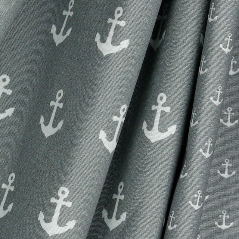 May include: Close-up of gray fabric with a repeating pattern of white anchors. The fabric is draped, showing folds and texture. The nautical theme is evident in the anchor design, suitable for home decor or apparel.