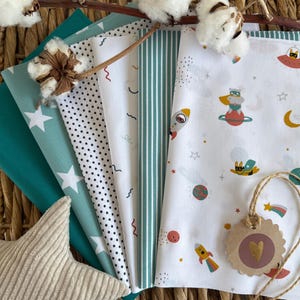 May include: A selection of fabric swatches in various patterns and colours, including teal, white, and space-themed prints. The patterns include stars, dots, and stripes. A beige star-shaped cushion and cotton sprigs are also visible.