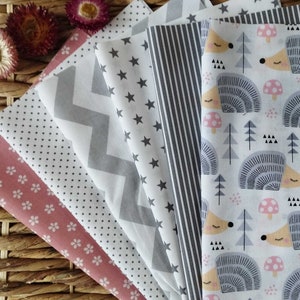 Könnte beinhalten: Ein Set aus sechs Stoffquadraten mit verschiedenen Mustern. Die Muster umfassen rosa Blumen, graue Punkte, graue Zickzacklinien, graue Sterne, graue Streifen und einen weißen Hintergrund mit grauen Igeln und Pilzen.