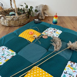 a colorful quilt with a polka dot pattern, a wicker basket, a stuffed elephant, and a stack of colorful stacking rings on a wooden floor.