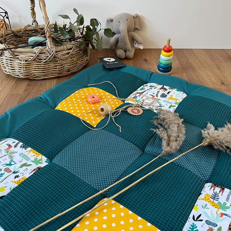 a colorful quilt with a polka dot pattern, a wicker basket, a stuffed elephant, and a stack of colorful stacking rings on a wooden floor.