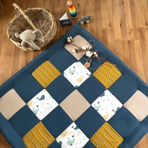 a quilt with a blue and yellow patchwork design, a basket with a stuffed animal, and various toys and accessories on a wooden floor.