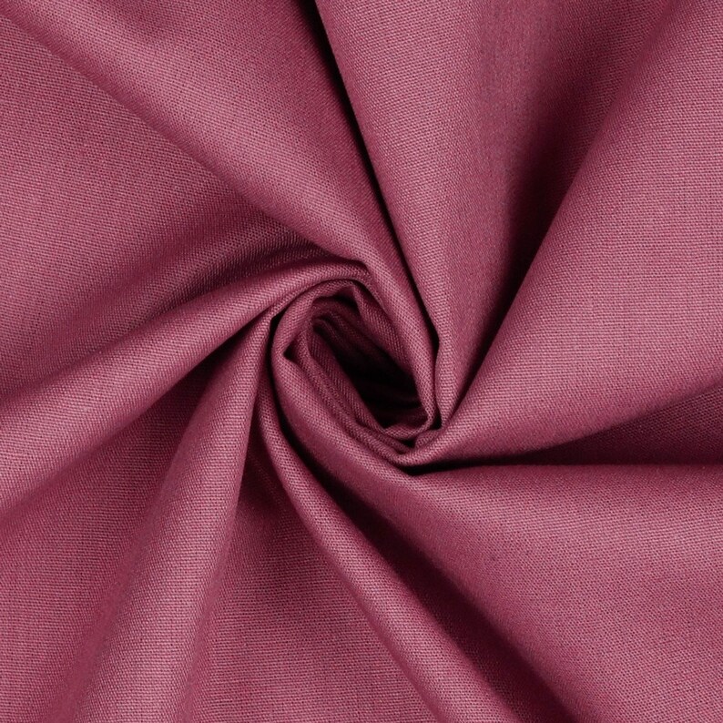 May include: Close-up of a soft, pink fabric with a smooth texture. The fabric is folded and draped, creating a swirling pattern.