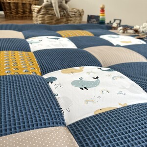 a close-up view of a quilt with a patchwork design featuring various colors and patterns, including a blue and white checkered pattern and a white and yellow pattern.