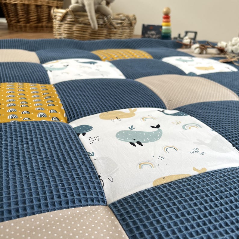 a close-up view of a quilt with a patchwork design featuring various colors and patterns, including a blue and white checkered pattern and a white and yellow pattern.