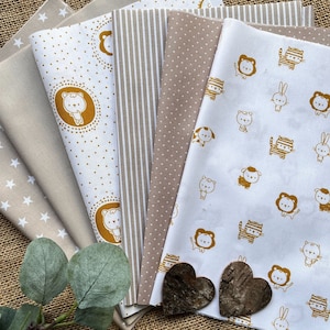 May include: A set of seven fabric squares with different patterns. The patterns include white stars on a beige background, white polka dots on a beige background, white stripes on a beige background, white polka dots on a beige background, a white background with gold animal illustrations, a white background with gold animal illustrations, and a white background with gold animal illustrations.