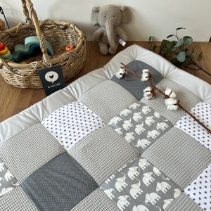 a cozy and inviting baby's room, with a gray and white elephant-themed quilt on the floor, a basket of toys, and a stuffed elephant toy.