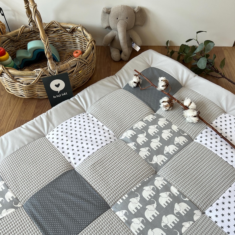 a cozy and inviting baby's room, with a gray and white elephant-themed quilt on the floor, a basket of toys, and a stuffed elephant toy.