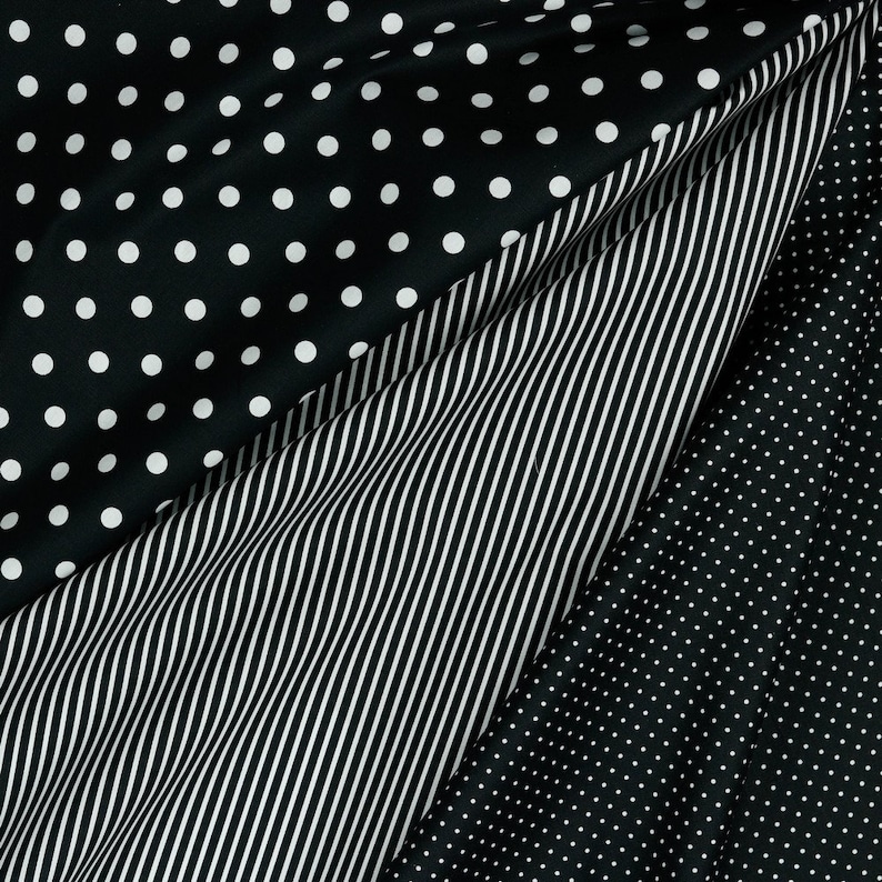May include: Black and white fabric with three different patterns: polka dots, stripes, and smaller polka dots. The fabric is folded to show all three patterns.
