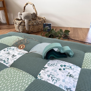 a cozy and inviting scene with a quilted green and white bedspread, a wicker basket, a stuffed elephant toy, and a greeting card on the floor.