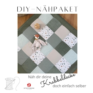 Könnte beinhalten: Ein Patchwork-Spielteppich für Babys mit verschiedenen grünen, weißen und beigen Quadraten. Ein kleiner Stofffuchs und ein geflochtener Ball liegen auf der Matte. Der Text "DIY-NÄHPÄKET" steht oben und "Näh dir deine Krabbeldecke doch einfach selber" unten.
