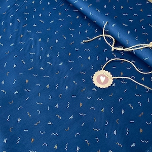 May include: Blue fabric with a white, yellow, and orange confetti pattern. The fabric is folded and a brown tag with a white heart is attached.