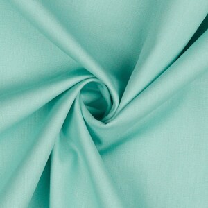 May include: A close-up of a soft, smooth, turquoise fabric. The fabric is folded and draped, showing its texture and color.