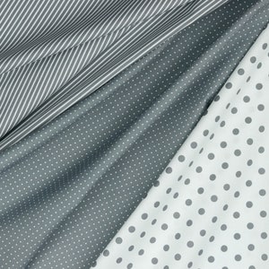 May include: Close-up of three different fabrics. One is white with gray stripes, another is gray with small white polka dots, and the third is white with large gray polka dots. The fabrics are draped and folded, showing their textures.