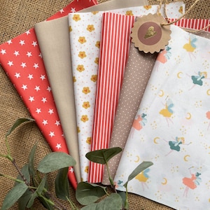 Könnte beinhalten: Ein Set aus sechs Stoffquadraten mit verschiedenen Mustern. Die Stoffe umfassen ein rot-weiß gestreiftes Muster, einen beigefarbenen Stoff mit kleinen weißen Punkten, einen weißen Stoff mit kleinen gelben Blumen, einen roten Stoff mit weißen Sternen, einen beigefarbenen Stoff mit einem Blumenmuster und einen weißen Stoff mit einem Feenmuster.