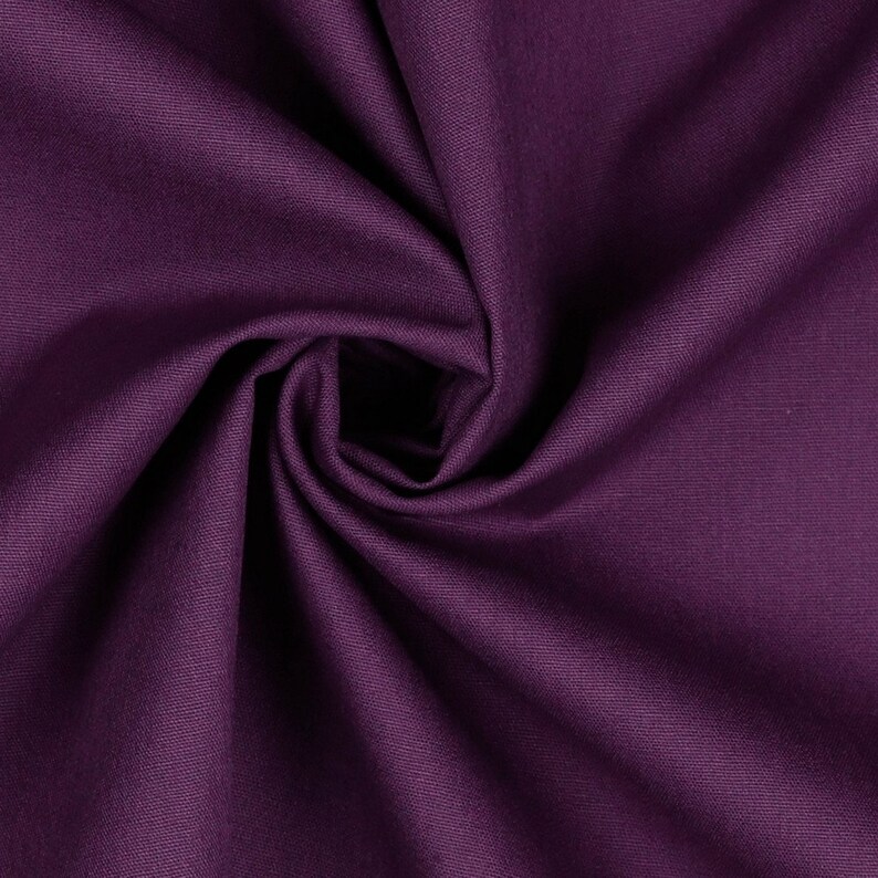 May include: A close-up of a deep purple fabric with a smooth, textured surface. The fabric is folded and draped, creating soft folds and curves.