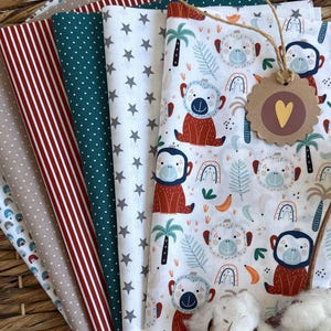 Könnte beinhalten: Eine Sammlung farbenfroher Stoffmuster in einem geflochtenen Korb. Muster umfassen rote Streifen, weiße Sterne, grüne Punkte und einen weißen Druck mit Affen, Regenbogen und Palmen. Ein Anhänger mit einem Herz ist befestigt.