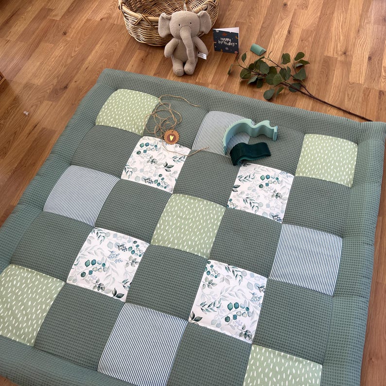 a quilt with a patchwork design, a stuffed elephant toy, and some decorative elements on a wooden floor.