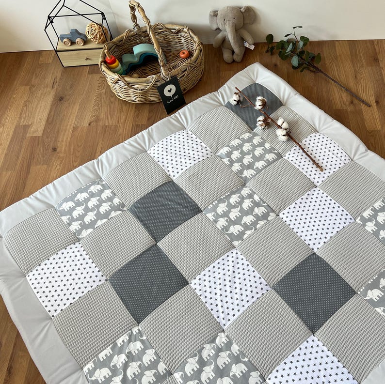 a quilt with a patchwork design of gray and white squares, along with a basket of toys and a stuffed elephant on a wooden floor.