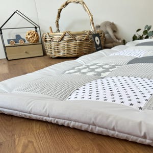 a cozy and inviting bedroom scene, featuring a gray and white quilt-like bedspread with a patchwork design, a wicker basket, and a small wooden toy car.