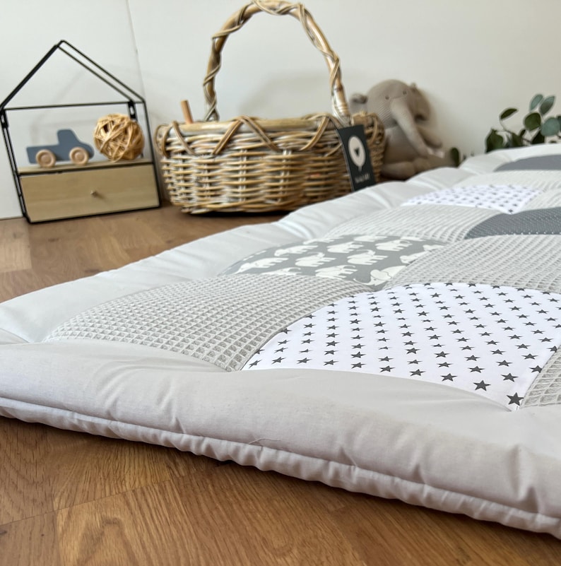 a cozy and inviting bedroom scene, featuring a gray and white quilt-like bedspread with a patchwork design, a wicker basket, and a small wooden toy car.