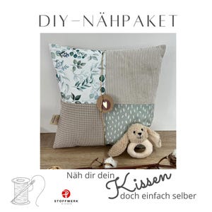 May include: DIY sewing kit for a pillow with a green and white floral pattern, a beige textured fabric, and a light green fabric with white dots. The kit includes a small stuffed animal and a ring for a baby.