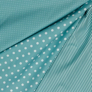 May include: A teal fabric with two different patterns. One side has large white polka dots on a teal background. The other side has small white dots on a teal background. The fabric is folded to show both patterns.
