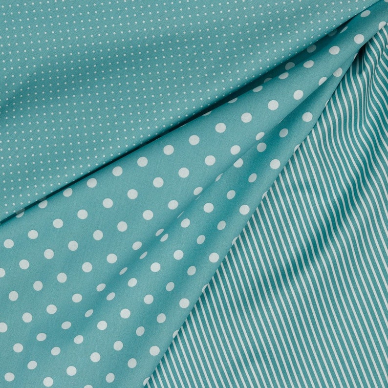 May include: A teal fabric with two different patterns. One side has large white polka dots on a teal background. The other side has small white dots on a teal background. The fabric is folded to show both patterns.