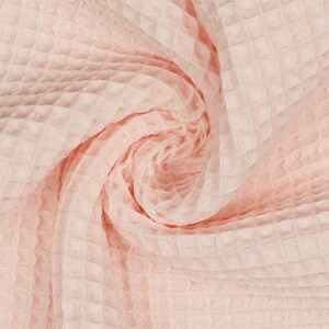 May include: A close-up of a soft, pink waffle weave fabric. The fabric is textured and has a subtle sheen.